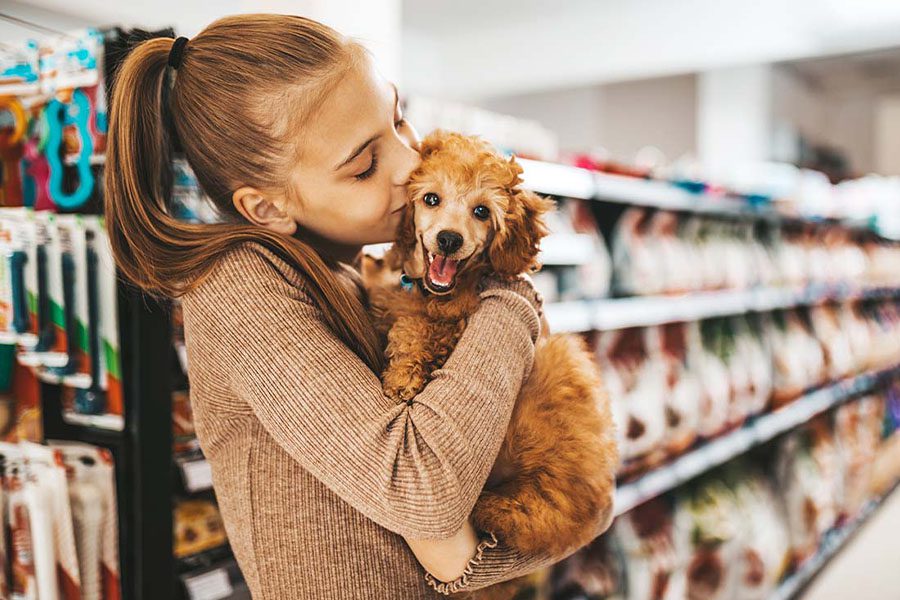Pet-Business-Insurance-Young-and-Joyful-Girl-Shopping-in-a-Pet-Store-with-Her-New-Poodle-Puppy-and-Giving-Him-with-a-Kiss